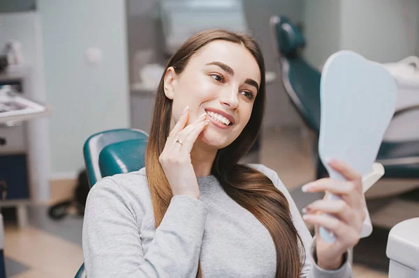 woman looking at her teeth with a handheld mirror