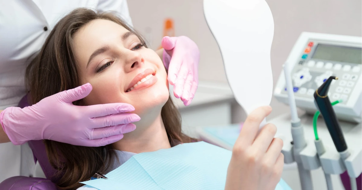 Patient smiling while reviewing her teeth in a dental mirror during a cosmetic dentistry consultation
